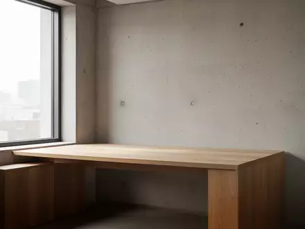 Ein minimalistischer Arbeitsbereich mit einem leeren Holztisch vor einer strukturierten Betonwand bei natürlichem Licht. - Foto: über boerse-global.de