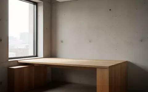 Ein minimalistischer Arbeitsbereich mit einem leeren Holztisch vor einer strukturierten Betonwand bei natürlichem Licht. - Foto: über boerse-global.de