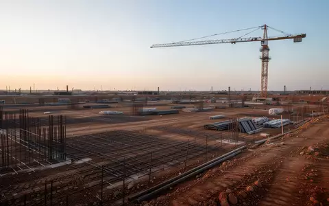 Eine weitläufige Baustelle mit Baustahlmatten und einem Baukran auf einer planierten Fläche bei Tagesanbruch. - Foto: über boerse-global.de