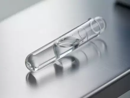 Ein Labor-Reagenzglas mit einer klaren Flüssigkeit auf einer metallischen Oberfläche, das die medizinische Diagnostik symbolisiert. - Foto: über boerse-global.de