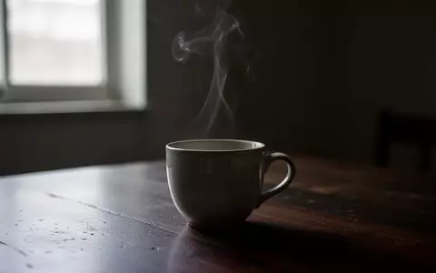 Eine dampfende Tasse auf einem dunklen Holztisch im gedimmten Licht. - Foto: über boerse-global.de