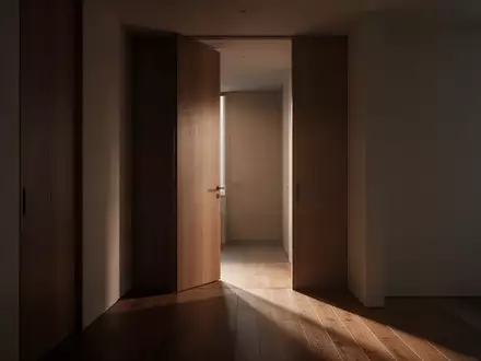 Ein minimalistischer, unmöblierter Flur in einer Wohnung mit einer leicht geöffneten Holztür und sanftem Lichteinfall. - Foto: über boerse-global.de