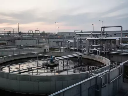 Moderne industrielle Kläranlage mit großen runden Sedimentationsbecken und komplexen Rohrleitungssystemen bei Dämmerung. - Foto: über boerse-global.de