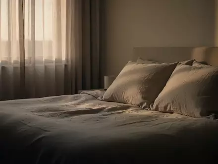 Ein minimalistisch eingerichtetes Schlafzimmer bei Tagesanbruch mit weichem, natĂĽrlichem Licht auf einer ungemachten Bettdecke. - Foto: ĂĽber boerse-global.de