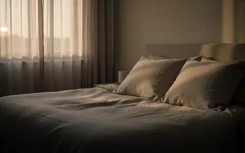 Ein minimalistisch eingerichtetes Schlafzimmer bei Tagesanbruch mit weichem, natürlichem Licht auf einer ungemachten Bettdecke. - Foto: über boerse-global.de