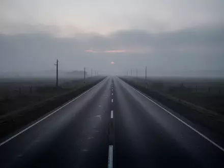 Eine leere, verlassene Asphaltstraße erstreckt sich in den nebligen Horizont bei Dämmerung. - Foto: über boerse-global.de