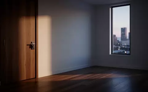 Ein schlicht eingerichteter Raum in einem Apartment mit Fokus auf eine geschlossene Tür und ein Fenster mit Stadtblick. - Foto: über boerse-global.de