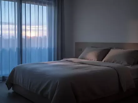 Ein ruhiges, minimalistisches Schlafzimmer bei Morgendämmerung mit weichem Tageslicht, das durch Vorhänge fällt. - Foto: über boerse-global.de