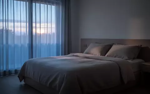 Ein ruhiges, minimalistisches Schlafzimmer bei Morgendämmerung mit weichem Tageslicht, das durch Vorhänge fällt. - Foto: über boerse-global.de