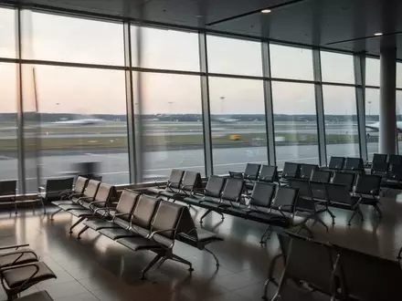 Leere Sitzreihen in einem modernen Flughafen-Terminal vor einer großen Fensterfront bei Morgenlicht. - Foto: über boerse-global.de