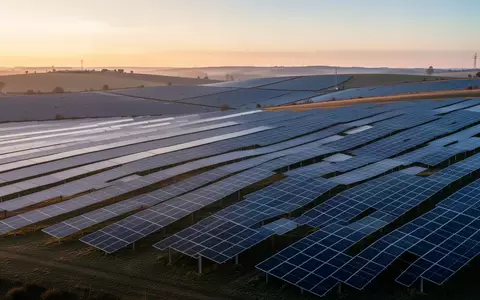 Weitläufige Solarparkanlage mit zahlreichen Photovoltaikmodulen bei Sonnenaufgang in einer hügeligen Landschaft. - Foto: über boerse-global.de