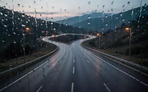 Eine leere, kurvige Bergstraße in der Abenddämmerung, gesehen durch eine verregnete Fensterscheibe. - Foto: über boerse-global.de