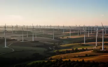 Weitläufige Windkraftanlagen in einer ländlichen Hügellandschaft bei Sonnenuntergang. - Foto: über boerse-global.de