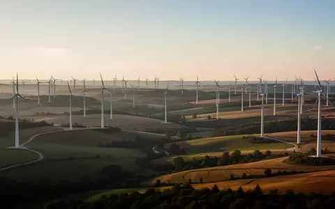 Weitläufige Windkraftanlagen in einer ländlichen Hügellandschaft bei Sonnenuntergang. - Foto: über boerse-global.de