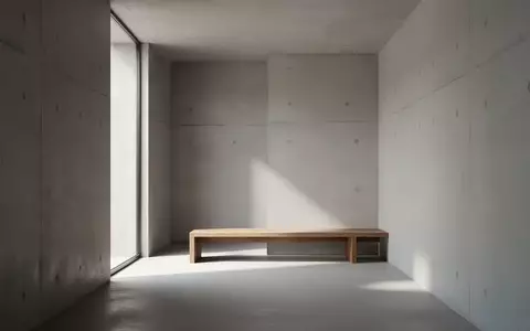 Ein minimalistischer, moderner Innenraum mit schlichten Betonwänden und weichem Tageslicht auf einer leeren Holzbank. - Foto: über boerse-global.de
