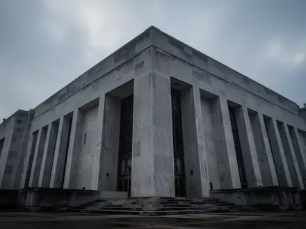 Eine monumentale, graue Betonfassade eines Regierungsgebäudes unter einem bewölkten Himmel. - Foto: über boerse-global.de