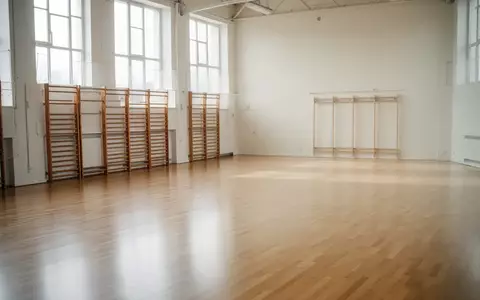 Leere, helle Sporthalle mit Parkettboden und Sprossenwand an einer weißen Wand. - Foto: über boerse-global.de