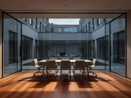 Ein minimalistischer, leerer Büro-Konferenzraum mit bodentiefen Fenstern und Blick auf einen ruhigen Innenhof. - Foto: über boerse-global.de