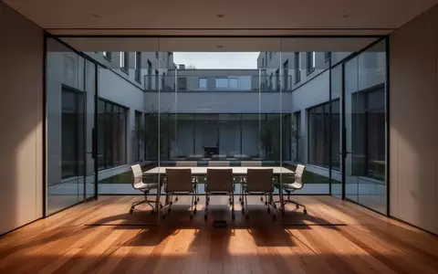 Ein minimalistischer, leerer Büro-Konferenzraum mit bodentiefen Fenstern und Blick auf einen ruhigen Innenhof. - Foto: über boerse-global.de