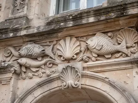 Detailaufnahme einer historischen Gebäudefassade mit Steinmetzarbeiten in Form von Fisch- und Muschelornamenten. - Foto: über boerse-global.de
