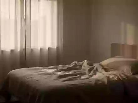 Ein minimalistisch eingerichtetes Schlafzimmer bei Tagesanbruch mit sanftem, natürlichem Licht, das durch einen Vorhang fällt. - Foto: über boerse-global.de