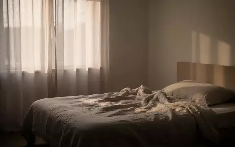 Ein minimalistisch eingerichtetes Schlafzimmer bei Tagesanbruch mit sanftem, natürlichem Licht, das durch einen Vorhang fällt. - Foto: über boerse-global.de