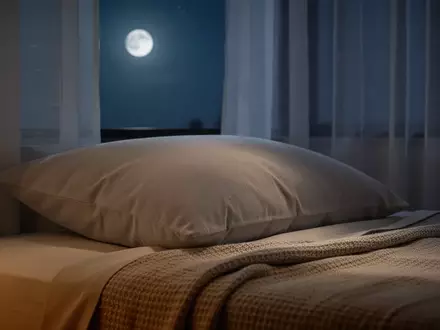 Ein ruhiges, minimalistisches Schlafzimmer bei Nacht mit sanftem Mondlicht, das auf ein bequemes Kissen und Bettwäsche fällt. - Foto: über boerse-global.de