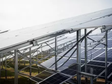 Reihen von Photovoltaikmodulen in einem großen Solarpark unter einem bewölkten Himmel. - Foto: über boerse-global.de
