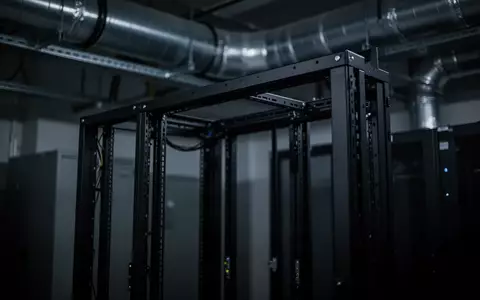 Ein dunkler, abstrakt gehaltener Serverraum mit leeren Rack-Gestellen und industrieller Belüftung in gedimmtem Licht. - Foto: über boerse-global.de