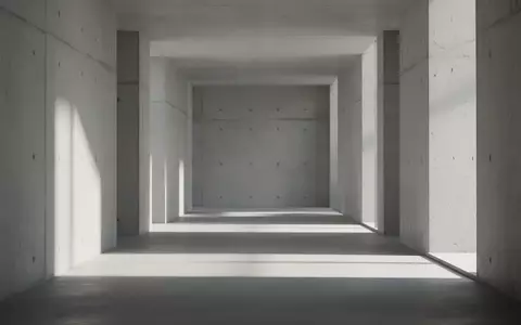 Ein minimalistischer, leerer Flur mit klaren Betonwänden und sanftem, natürlichem Licht, der eine ruhige architektonische Umgebung darstellt. - Foto: über boerse-global.de