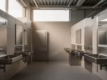Ein moderner, minimalistisch gestalteter Sanitärraum in einem Industriebetrieb mit neutralen Fliesen und Edelstahlarmaturen. - Foto: über boerse-global.de