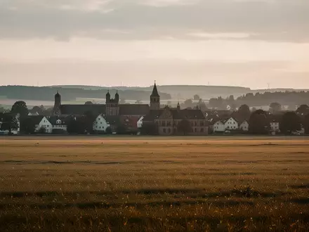 Weite, ruhige Landschaft mit Feldern und im Hintergrund sichtbarer, historischer Bebauung in Deutschland bei goldenem Licht. - Foto: über boerse-global.de