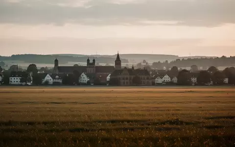 Weite, ruhige Landschaft mit Feldern und im Hintergrund sichtbarer, historischer Bebauung in Deutschland bei goldenem Licht. - Foto: über boerse-global.de