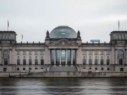 Das Gebäude des Deutschen Bundestages unter einem bewölkten Himmel mit Blick auf die Glaskuppel. - Foto: über boerse-global.de