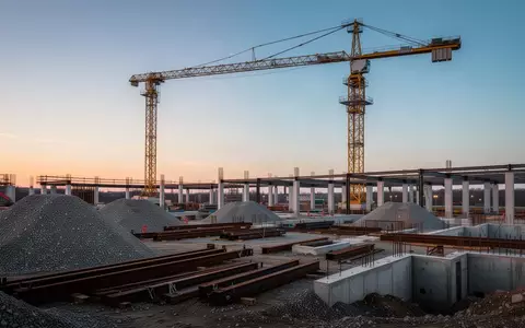 Eine Baustelle mit einem gelben Baukran und Fundamenten für ein großes Infrastrukturprojekt bei Sonnenuntergang. - Foto: über boerse-global.de