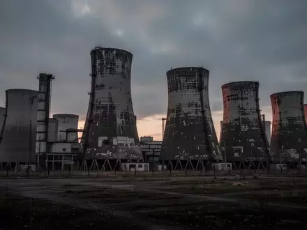 Industrielle Architektur mit großen Kühltürmen in einer kargen Landschaft bei Dämmerung. - Foto: über boerse-global.de