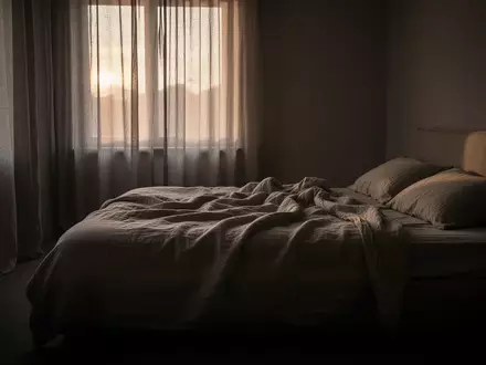 Ein ungemachtes Bett in einem spärlich beleuchteten Schlafzimmer im Morgengrauen, das eine Atmosphäre der Erschöpfung vermittelt. - Foto: über boerse-global.de
