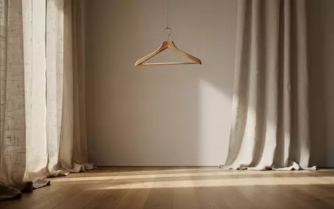 Ein minimalistisch eingerichteter Ankleideraum mit einem leeren Holzkleiderbügel und hellen Leinenvorhängen. - Foto: über boerse-global.de