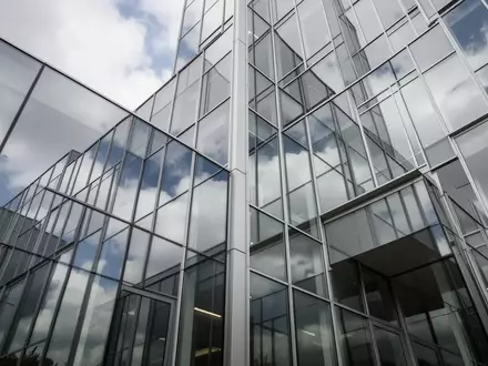 Moderne Glasfassade eines Bürogebäudes mit Spiegelungen des Himmels und architektonischen Linien. - Foto: über boerse-global.de