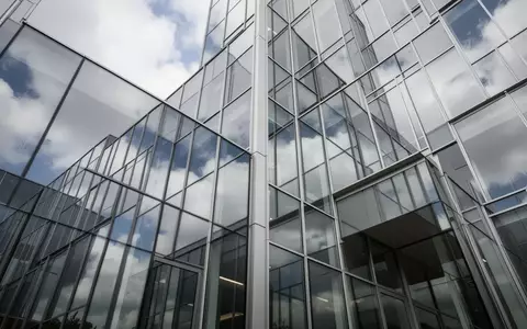 Moderne Glasfassade eines Bürogebäudes mit Spiegelungen des Himmels und architektonischen Linien. - Foto: über boerse-global.de