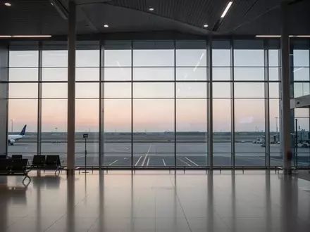 Ein minimalistischer, menschenleerer Abflugbereich an einem Flughafen in der Abenddämmerung mit Blick auf das Rollfeld. - Foto: über boerse-global.de
