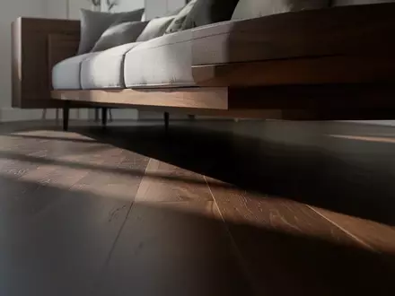 Ein schmaler Spalt unter einem modernen Sofa auf einem dunklen Holzboden in einem minimalistischen Wohnzimmer. - Foto: über boerse-global.de