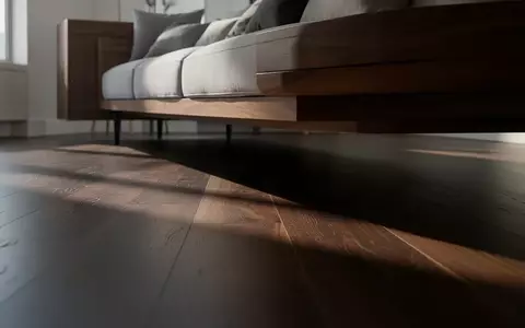 Ein schmaler Spalt unter einem modernen Sofa auf einem dunklen Holzboden in einem minimalistischen Wohnzimmer. - Foto: über boerse-global.de
