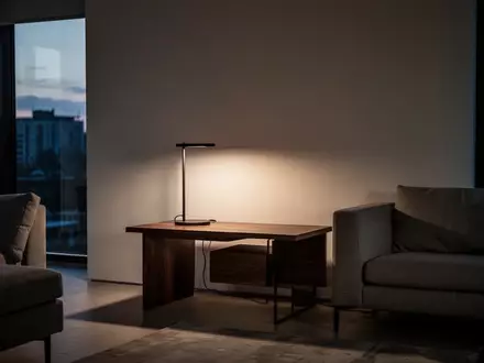 Ein minimalistisch eingerichteter Wohnraum mit gedimmtem Licht und einem modernen Beistelltisch vor einer leeren Wand. - Foto: über boerse-global.de
