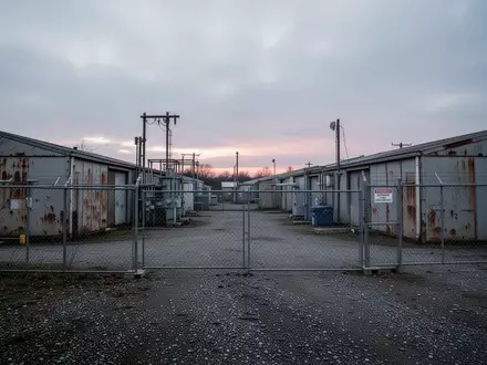 Ein umzäunter städtischer Betriebshof mit mehreren schlichten Wirtschaftsgebäuden und Lagerhallen an einem bewölkten Tag. - Foto: über boerse-global.de