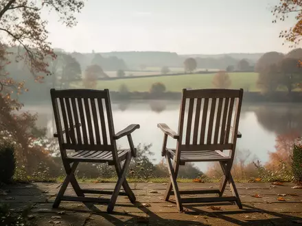 Zwei leere Gartenstühle auf einer Terrasse mit Blick in eine herbstliche Landschaft als Symbol für soziale Teilhabe im Alter. - Foto: über boerse-global.de