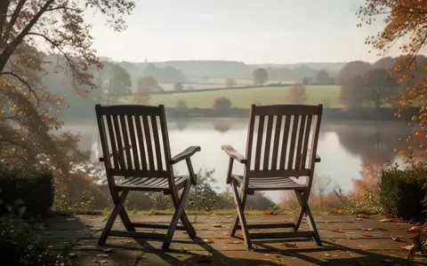 Zwei leere Gartenstühle auf einer Terrasse mit Blick in eine herbstliche Landschaft als Symbol für soziale Teilhabe im Alter. - Foto: über boerse-global.de