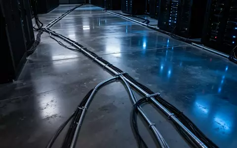 Dunkler, minimalistischer Serverraum mit kühler blauer Beleuchtung und industriellen Kabelkanälen am Boden. - Foto: über boerse-global.de