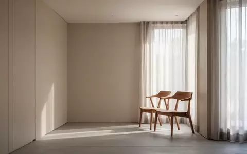 Ein minimalistisch eingerichteter, heller Raum mit einem leeren Holzstuhl vor einem Fenster mit lichtdurchlässigen Vorhängen. - Foto: über boerse-global.de