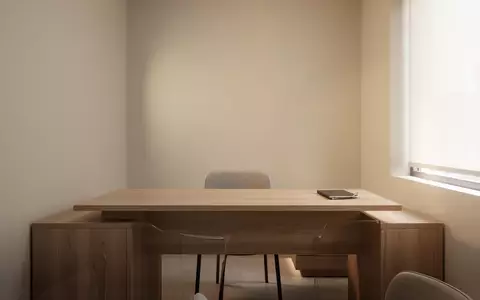 Ein minimalistisch eingerichteter, heller Behandlungsraum in einer Arztpraxis mit einem leeren Stuhl vor einem Holztisch. - Foto: über boerse-global.de